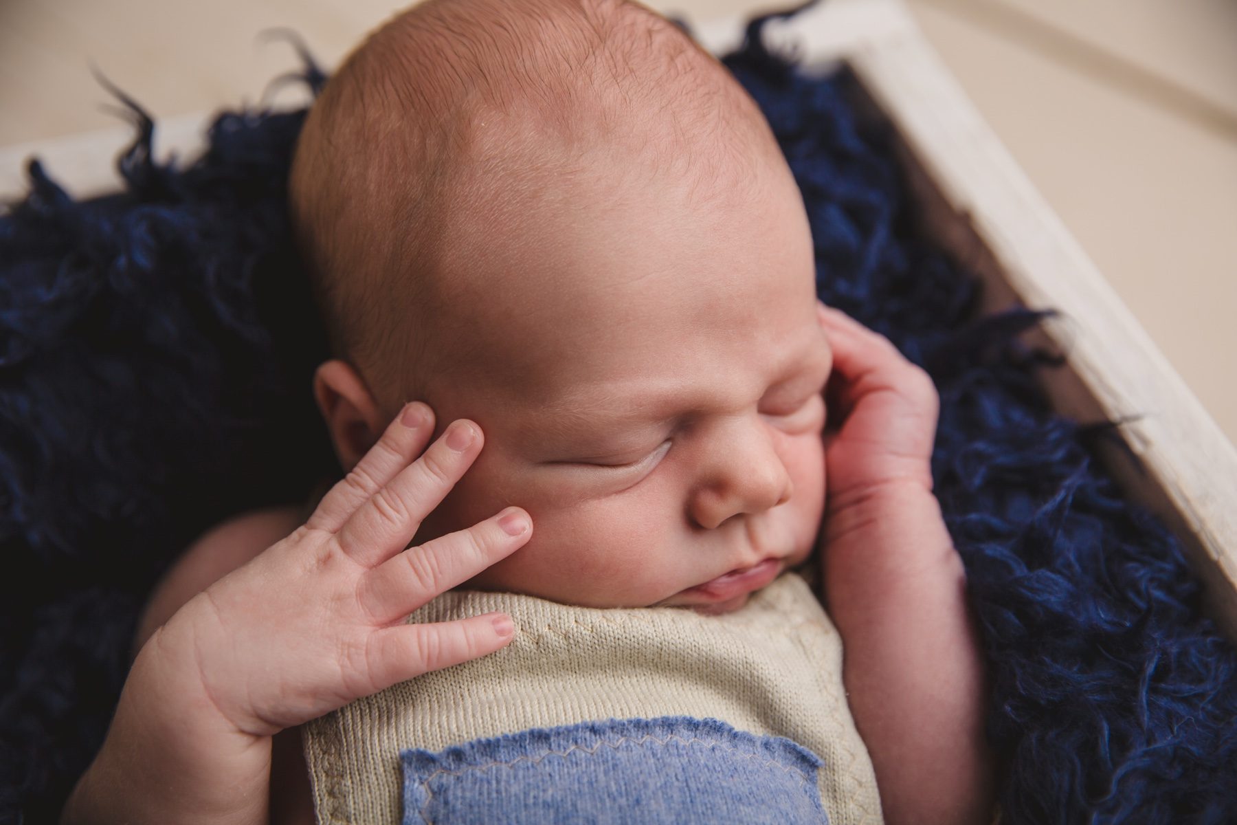 Ein schlafender Säugling liegt mit der Hand an der Wange auf einer blauen Decke